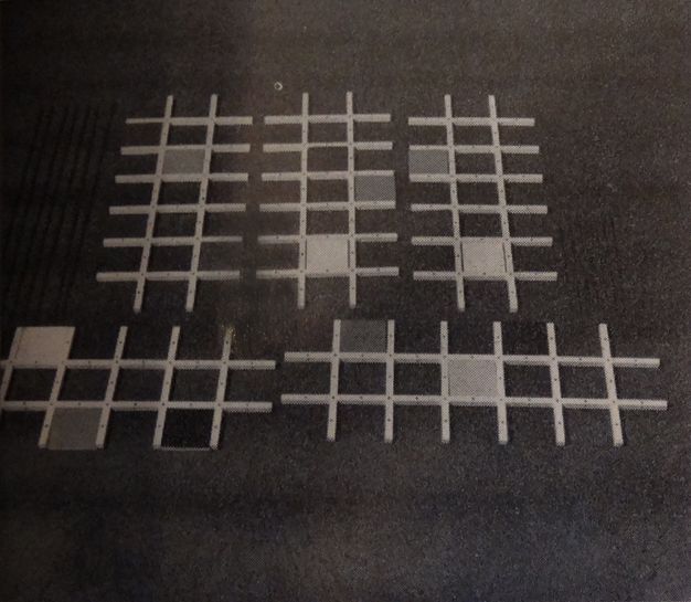 Sculpture. Six lattices, like pieces of a trellis, lie against a dark ground. Each is made of two long rows overlapping six shorter rows, like an elongated tic-tac-toe board. Each piece has one, two, or three cells filled in with solid squares in varying shades.