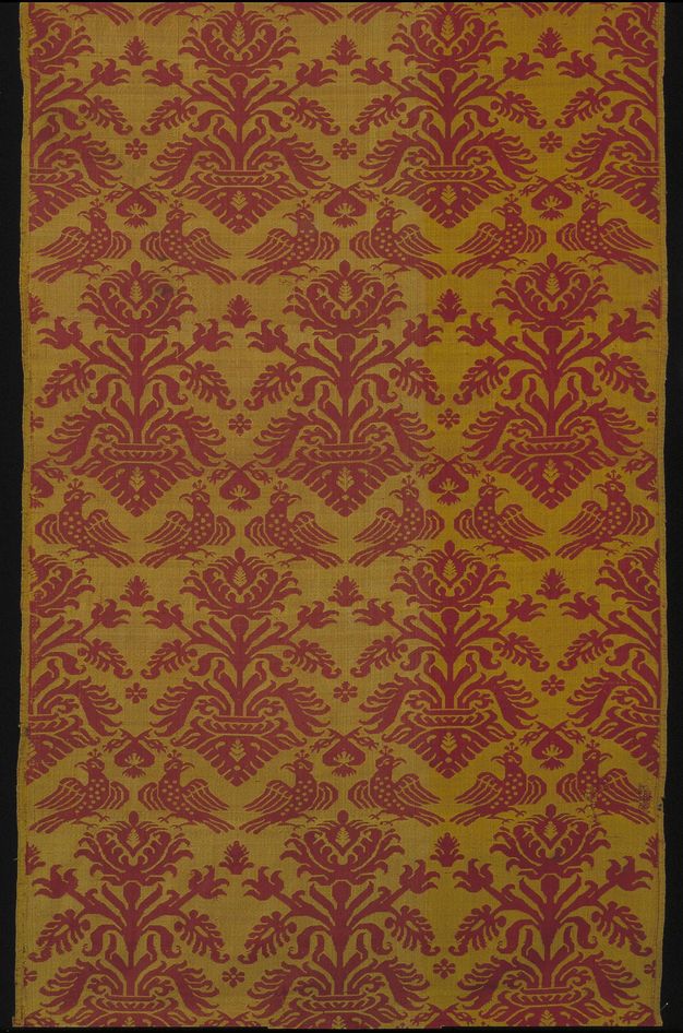 Textile. Stylized birds and flowers create a pattern in maroon red against a muted gold background.