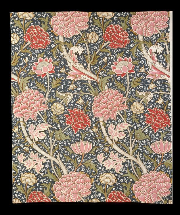 Textile. Petal-pink and red, stylized flowers grow on parchment-white stems with olive-green leaves to create a dense pattern. The background has a smaller pattern of white vines against deep blue.
