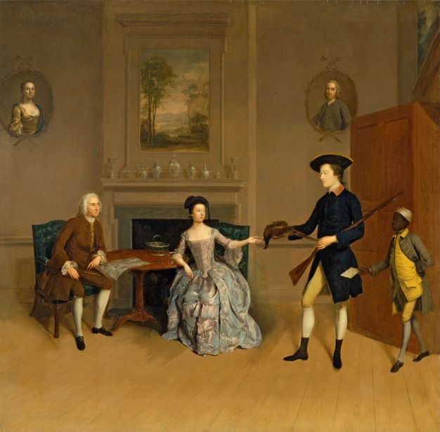 Painting. A man and woman sit at a round table in front of a hearth as a younger man brings and presents a game bird, a rifle tucked in one elbow. A brown-skinned man is smaller in scale behind the younger man. The three others and two oval portraits hanging to each side of the hearth all have pale skin.