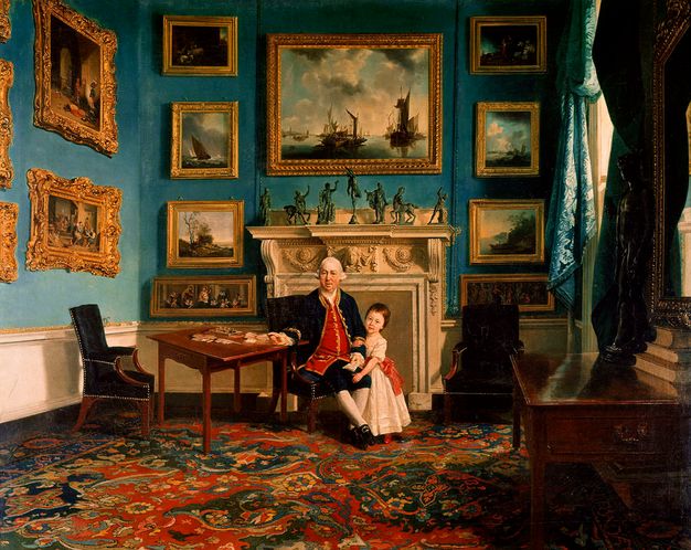 Painting. An older man with sagging jowls and bags under his eyes sits at a letter-writing table in front of a hearth. A young child stands by his knee and hooks one hand around the older man’s arm. Seven bronze statuettes line the mantle and genre paintings, land- and seascapes in carved, gilded frames fill the wall around the hearth.