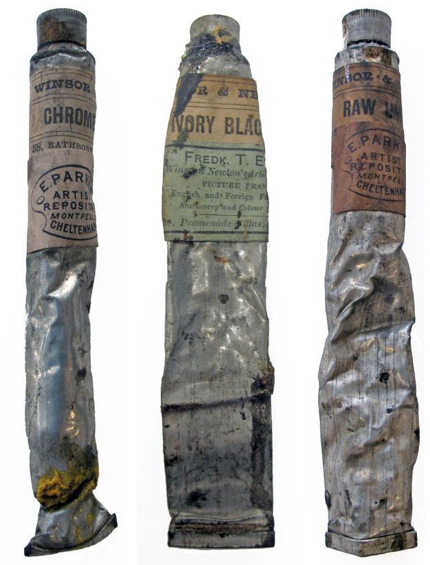 Three silver tubes of paint are partially crumpled. Each has a label near the top. From left to right, visible text reads “Winsor Chrome” on the first; “Ivory Black Fredk. T. E Winsor & Newton” at the centre; and “Windsor & Raw Um” to the right.