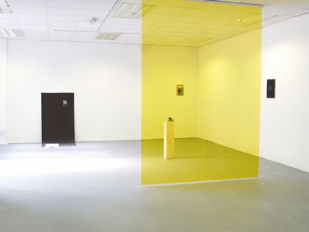 Installation. A translucent yellow panel hangs longways in front of us, so half the room beyond is seen as if through a yellow lens. Two works hang widely spaced on the wall beyond. A dark rectangular shape opposite us could be a doorway in the room or something black against the wall.