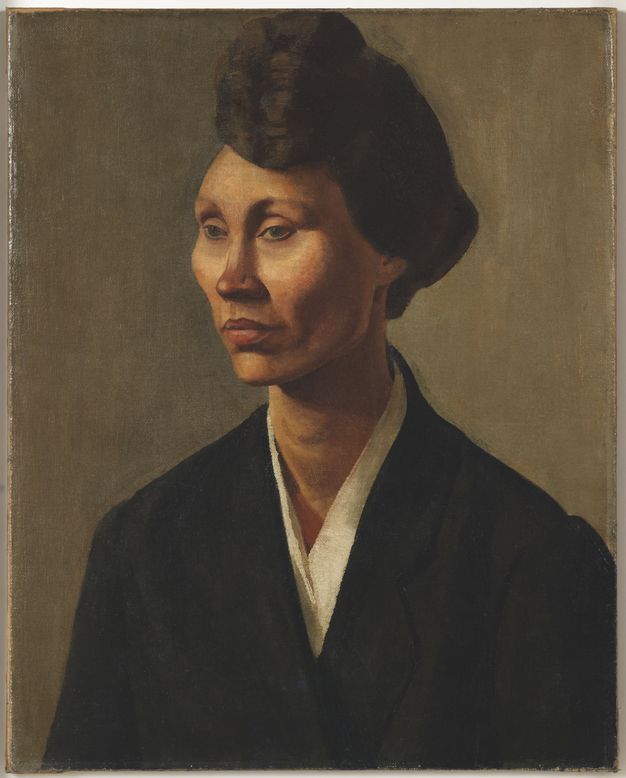 Painting. Shown from the chest up against an olive-green background, a woman looks off to our left with an unfocused gaze. Her eyes angle upwards under curved brows. She has high cheekbones, a narrow chin, and her full lips are set. Her skin is light tan with areas of dark pink around her cheekbones and nose, and paler areas under her eyes. She wears a black coat over a white shirt.