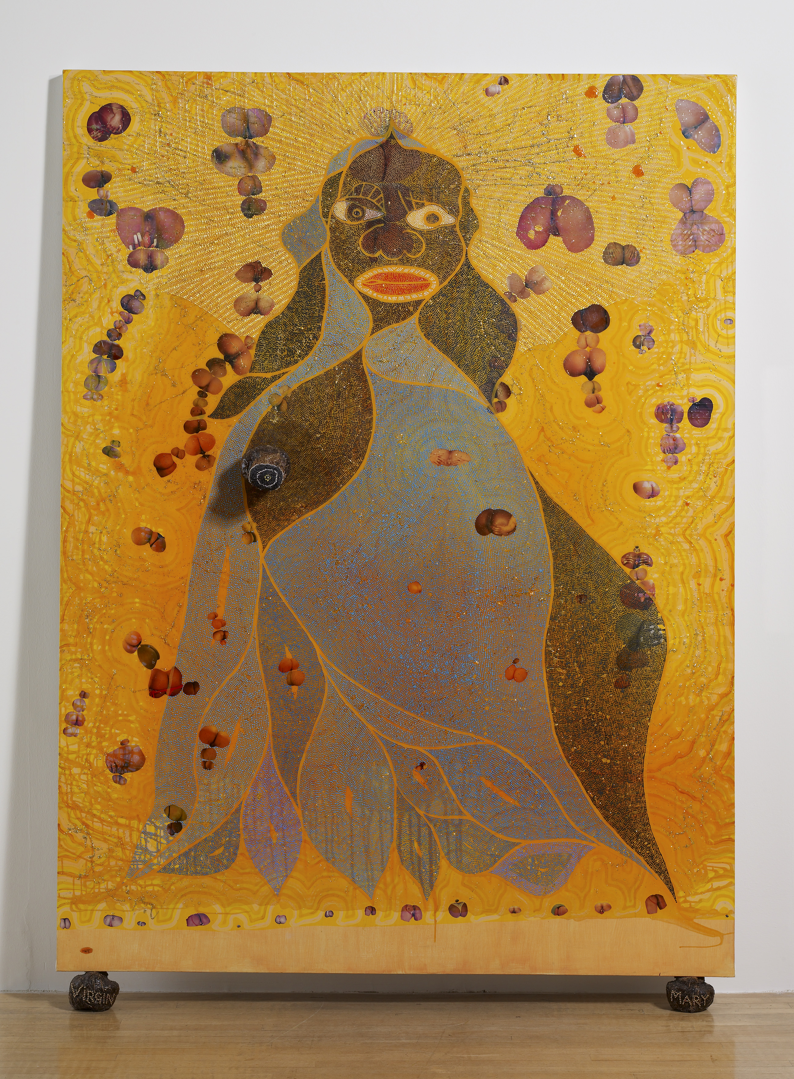 Painting. A woman with black skin, the Virgin Mary, has stylized features, including oval-shaped red lips and a wide nose. Close-up views of genitalia are collaged onto the gold background.