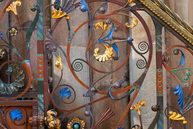 Railing. Curling, swirling ironwork is gold-coloured or painted brilliant blue, muted purple, pine green, or umber orange.