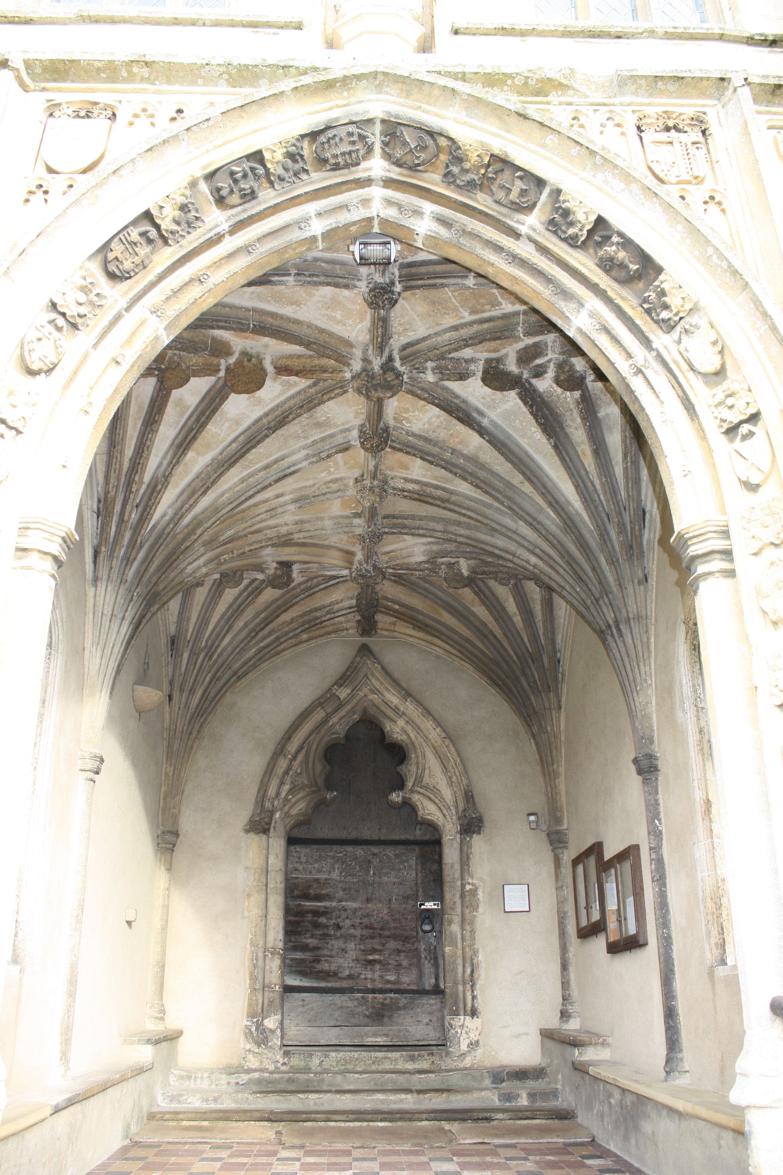 Architecture. We look up into the ribbed, vaulted ceiling of a porch projecting from the side of a church. The opening, close to us, is a pointed arch.