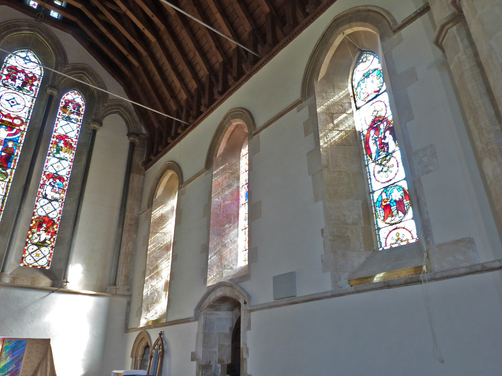 Architecture. Light pours through tall stained glass windows under the timbred ceiling of this church. The lowest level has an arched niche near the corner and doorway a little farther along the wall.