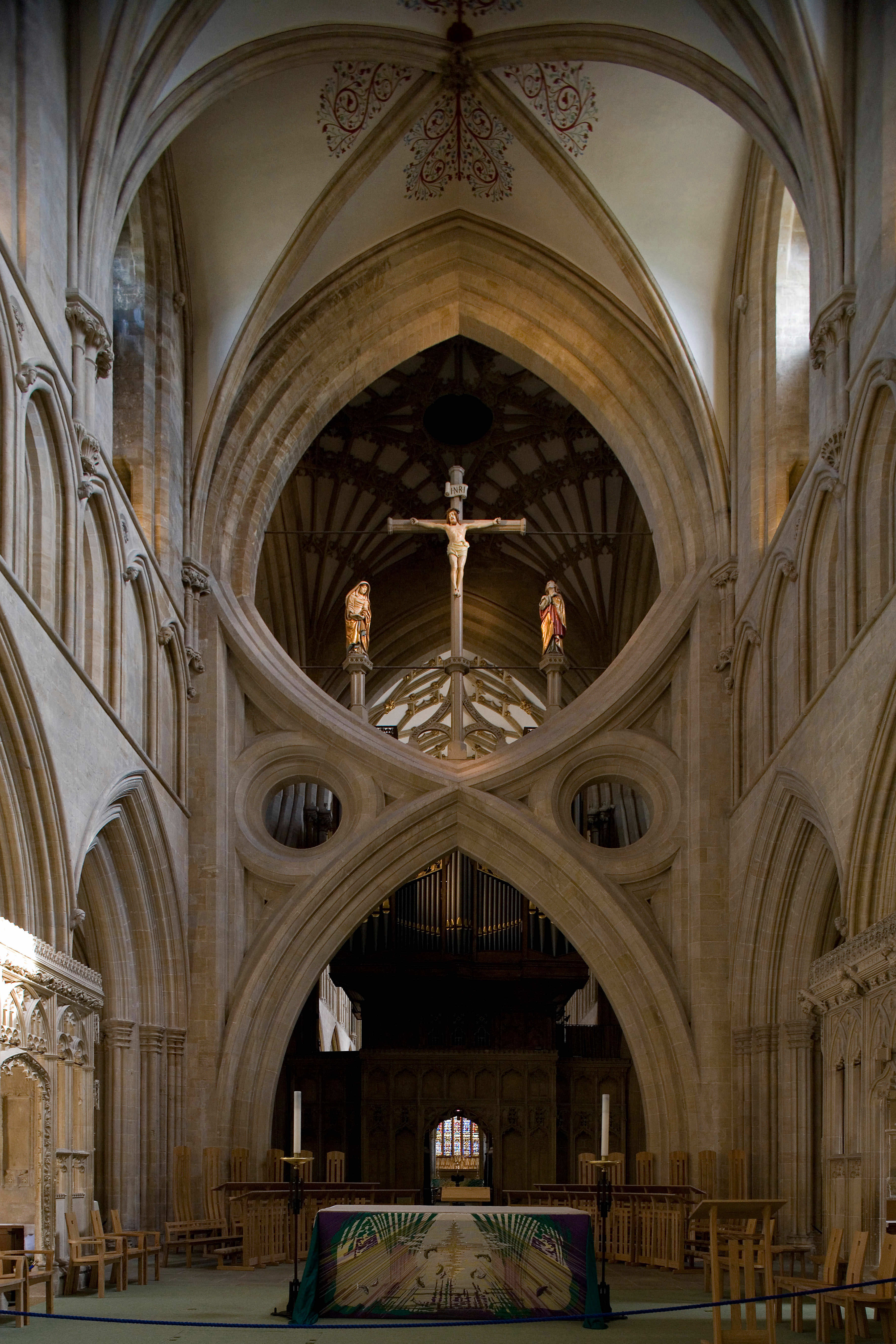 Architecture. Mirrored arches, one opening up and one opening down, resemble an hourglass with empty spandrels, like eyes, to each side. A crucifix and statues of the Virgin Mary and St John the Evangelist are framed in the upper half of the hourglass.