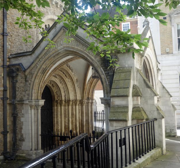 Architecture. An arched stone porch extends from an arched doorway, which is lined with the nested arches of the archivolt on the side of a church. The porch has a slightly pointed arch on the side we see the most clearly.
