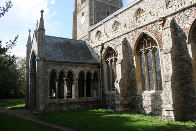 Architecture. A covered porch extends from the side of a stone church so the opening faces our left. The porch wall facing us is pierced with two windows, each of which is made up of three narrow pointed arches.