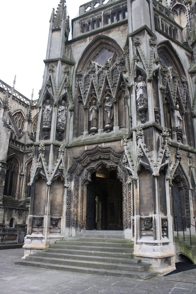 Architecture. A lavishly carved and ornamented porch extends from the side of a stone Church. Stairs lead up to the opening which is arched, but segmented into three, bracket-like lobes.