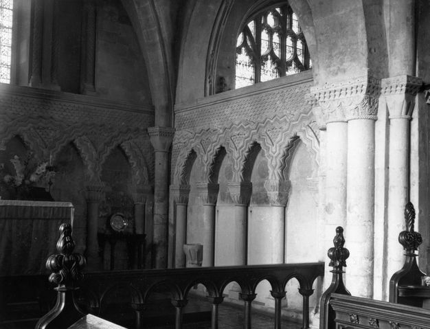 Architecture. Black and white photograph of a corner of a stone church with wide, pointed arches. Rows of blind overlapping arches line the two walls shown here. The arches are decorated with bands of zig zags.