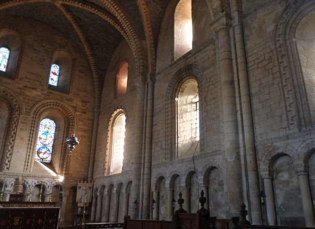 Architecture. We look into the soaring corner of a stone church with monumental arched bays. Rows of blind arches line the lowest level.