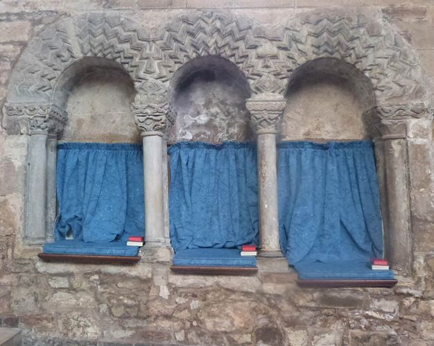 Architecture. Three arched niches set into a stone wall are hung with blue cloth and have blue cushions. The arches have rows of zig zags, giving the seats a somewhat electric look.