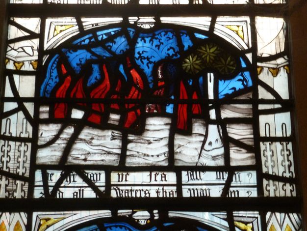 Stained glass window. Detail view of red flame-like tongues flicking up from white water in which fish swim.