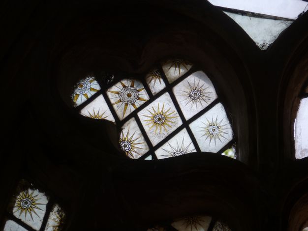 Stained glass window. Detail view of a leaf-shaped opening for stained glass. Diamond-shaped panes have gold sunbursts overlaid with stylized white roses.
