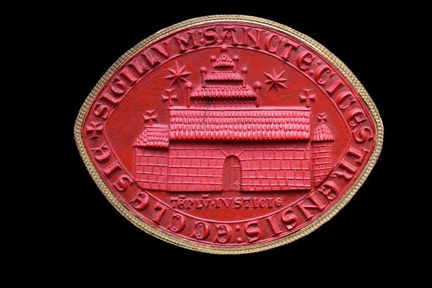 Seal. An impression of a seal made with red material shows a church, chancel, and freestanding tower. A three-stepped tower structure is above the long roof of the church. Two stars are in the sky. Latin text in all caps around the perimeter reads, “Sigillum: Sancte: Cicestrensis: Ecclesie”.