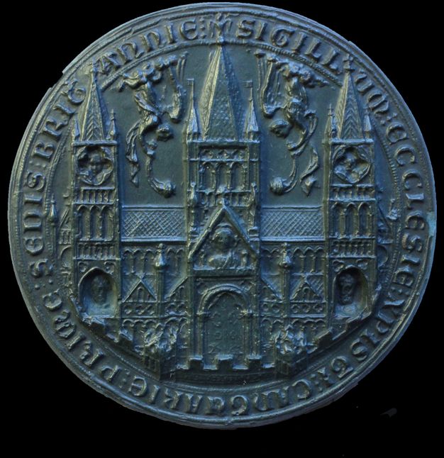 Seal. Cast of a round seal shows a church with three towers. Facing head-down, winged angels blow horns between the towers. Latin text lines the perimeter.