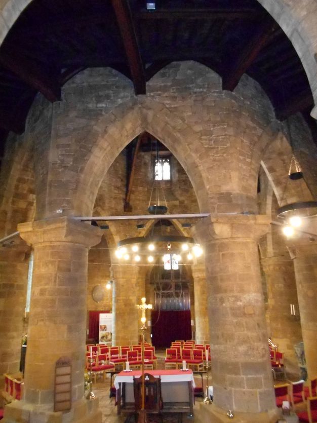 Architecture. Tall, pointed arches supported on wide columns enclose a circular nave inside a stone church. Red chairs are set up in rows facing an altar under the arch closest to us.
