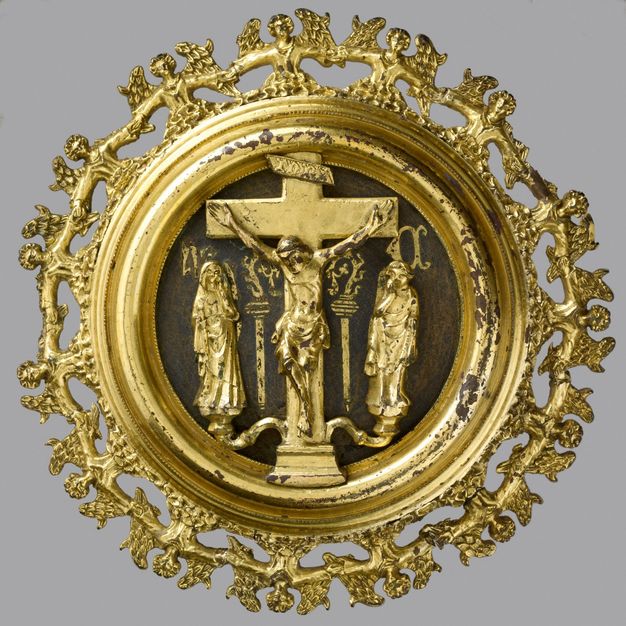 Plaque. A golden, medallion-like roundel shows the crucifixion attended by a robed woman and man, the Virgin Mary and St John the Evangelist. The perimeter is made up of a band of angels, shown hand-in-hand from the waist up.