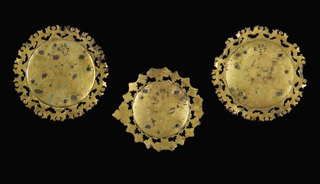 Plaques. The backs of three medallion-like roundels with decorated perimeters are shiny gold with a few dark spots.