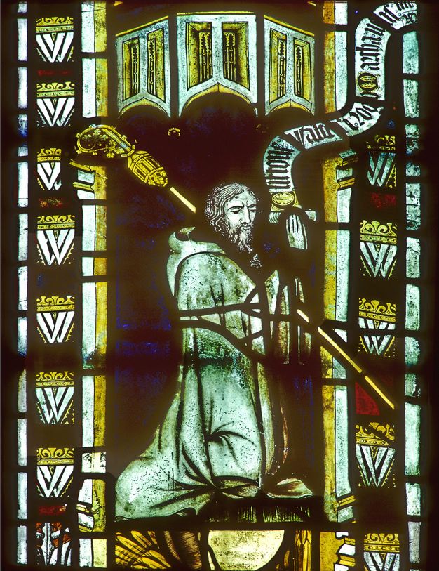 Stained glass window. Detail view of a man kneeling, facing to our right, and resting a hooked staff over one shoulder.