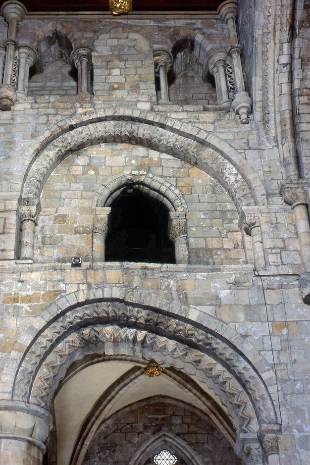 Architecture. Round arches within a three-storey bay of a church settled unevenly so they are noticeably distorted, as if the halves to our right had melted.