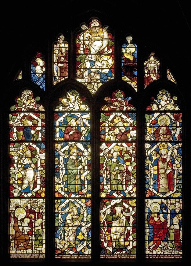 Stained glass window. Four columns of stained glass encased in pointed arches are enclosed within a larger pointed arch. Single people with scrolls with writing occupy most sections but a few show pairs or small groups of people.
