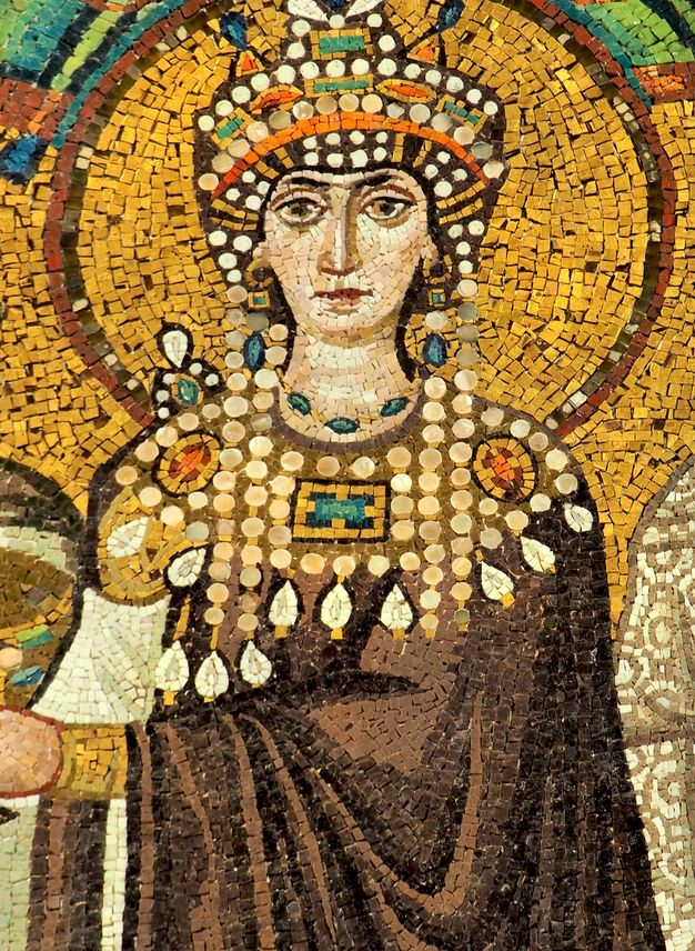 Mosaic. Detail view of a woman wearing a brown robe or cloak, a broad decorated collar and a jewelled headdress. She has pale skin, and her head is surrounded by a halo.