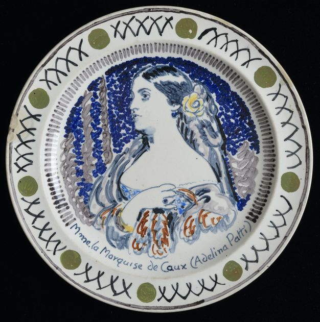 Plate. A woman holds one hand next to her oppositve shoulder as she looks off to our left, almost in profile. Her gleaming black hair is held back with a yellow flower. Her chest is an expanse of white above a low-cut bodice. Her name is painted below, \“Mme. la Marquise de Caux (Adelina Patti)\”.