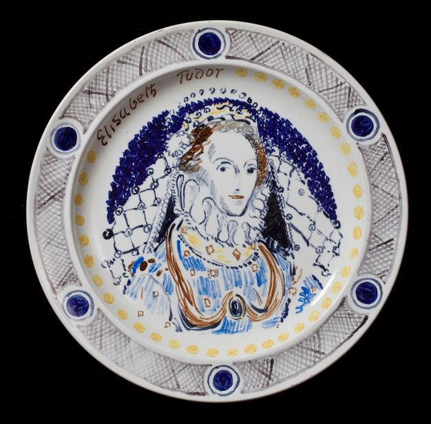 Plate. A woman wearing a crown and a high, ruffled collar looks sideways at us. A veil falls from the back of her crown to her jewelled dress. The portrait is painted mostly in tones of blue with some touches of brown, black and yellow. A ring of yellow dots runs just inside the rim of the plate, and her name is painted at the upper left, \“Elisabeth Tudor\”.