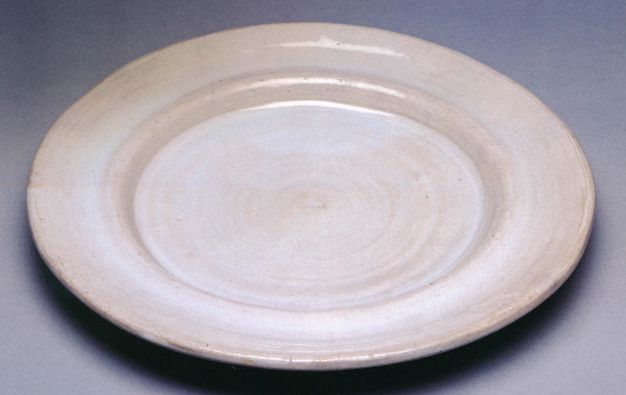 Plate. This white, earthenware plate has a slightly concave rim around a flat, round centre.