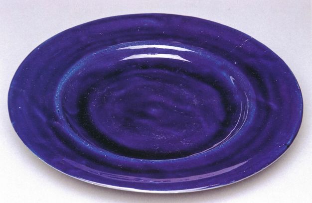 Plate. This cobalt-blue, earthenware plate has a slightly concave rim around a flat, round centre.