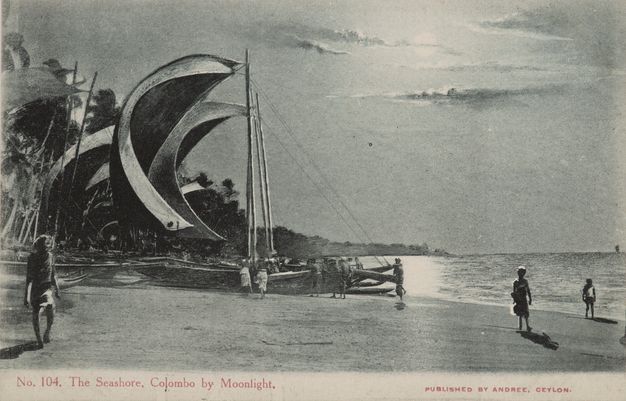 Black and white photograph. In this image reproduced on a postcard, moonlight warms the sky, and it reflects off water below. The sails of a sailboat puff full in the wind even though the boat is pulled onto a flat beach to our left.