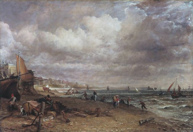 Painting. Waves lap against a beach under cloud-filled skies. A rowboat and at least one sailboat have been pulled up onto the beach to our left. Men and a dog sit and work there. More people walk along the beach, which angles from the lower right corner into the distance to our left. A line of buildings further up the shore blends into a distant bridge along the horizon, which comes about a third of the way up this canvas.