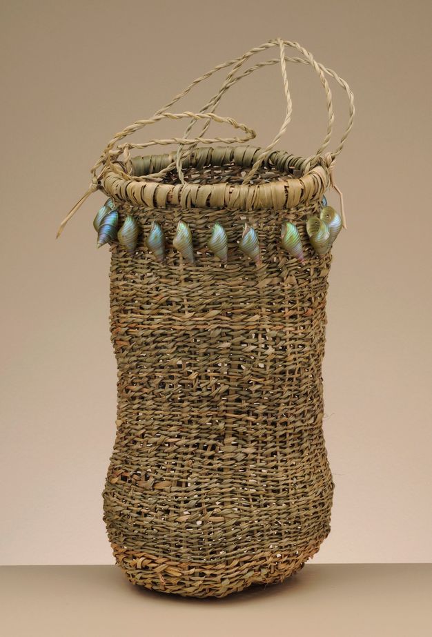Basket. Tall woven vessel has a rounded bottom and iridescent, spiralling shells around the mouth. Thin handles loop up from the top.