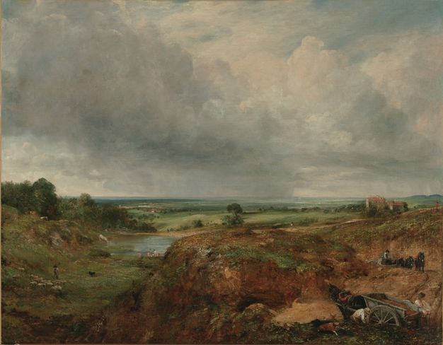 Painting. A pond nestles among in a grassy area beyond a flat-topped promontory in this landscape. The horizon comes just under halfway up this composition. Banks of steel-blue clouds sweep across the flat land above, and rain falls in the far distance.