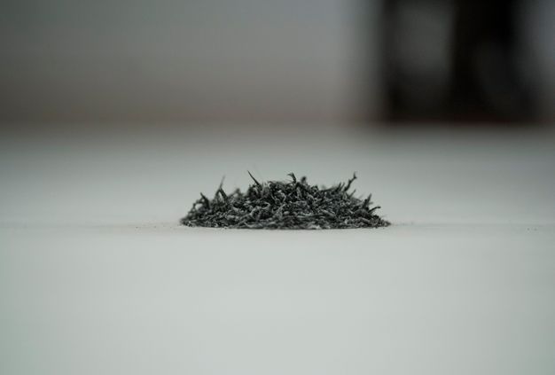Installation. Close up view of a pile of grey rubber eraser shavings. The space behind the pile quickly falls out of focus.