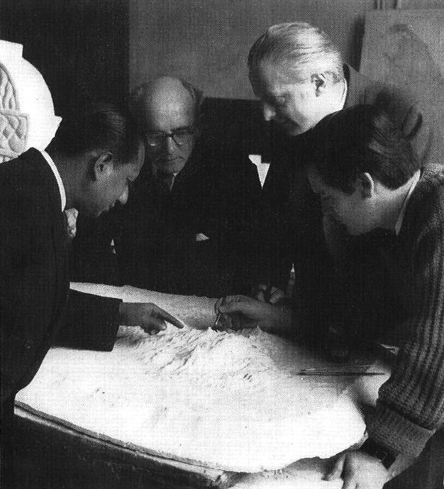 Black and white photograph. Four men gather around a white relief map.