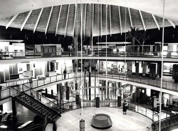 Architecture. Black and white photograph of an open, round, three-storey space. Each floor is lined with rooms, and balconies surround the open space.