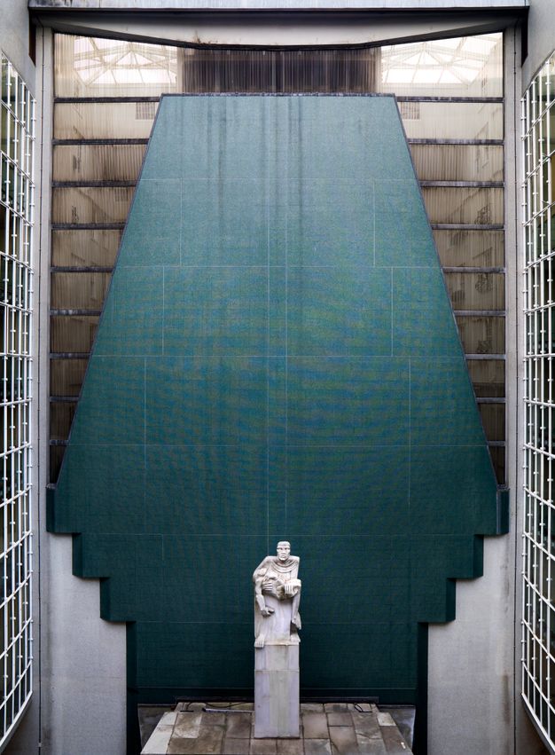 Architecture. An alcove is backed by blue stone that flares down from the top and then steps inwards to narrow at the bottom around a person holding the limp body of another.
