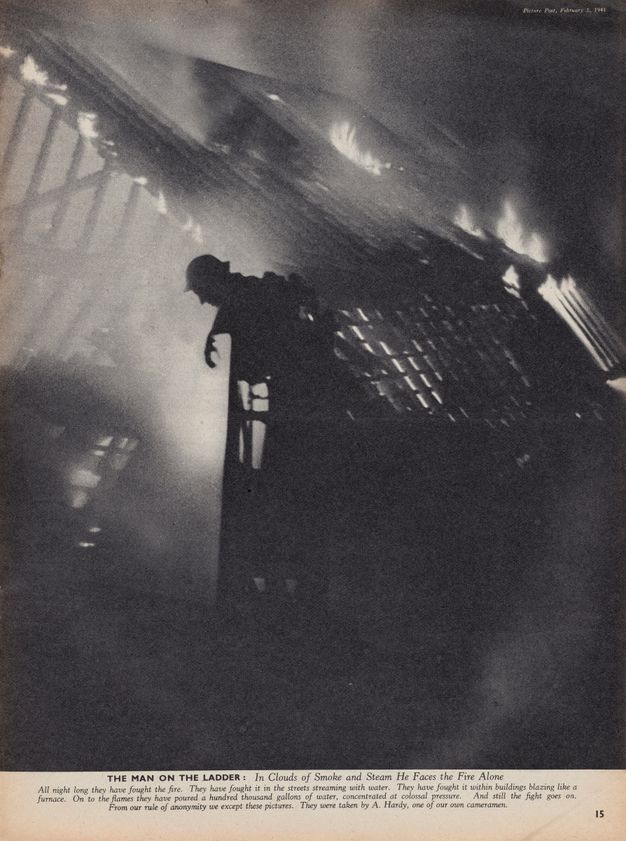 Magazine illustration. A man with a brimmed helmet leans out over a ladder against a burning building. The scene is shrouded in smoky haze. After the title, the caption below continues, “In Clouds of Smoke and Steam He Faces the Fire Alone”.