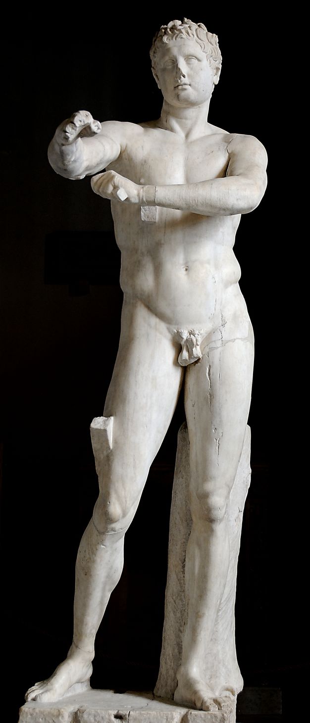 Sculpture. This freestanding statue of a clean shaven, muscular man is carved from white marble. Most of his weight is on his left leg. His left arm crosses his chest and he holds an object, now missing, near his other upper arm. That hand is raised and comes towards us in this photograph.