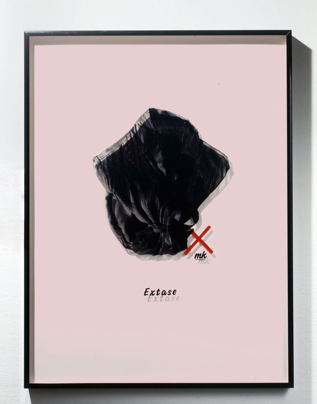 Mixed media. A photograph of a black, collared woman’s shirt or robe has been printed onto a piece of Plexiglass and mounted in a frame so it casts a shadow on the pastel pink mat behind it, creating double vision. The word “Extase” is below.