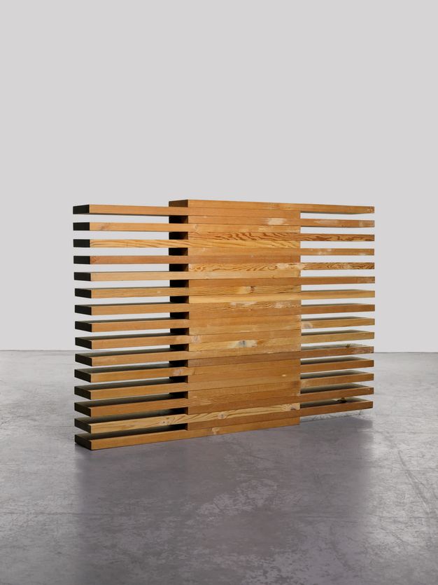 Sculpture. Thirty boards of honey-brown lumber are stacked one atop the other so half of each board overlaps the board below. This creates an alternating, comb-like appearance to each side of the solid stack.