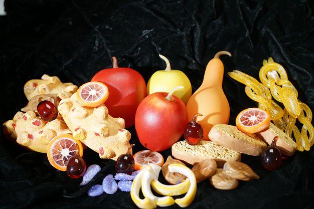 Glass. Apples, a pear, grapes or cherries, slices of orange, dried figs, candied lemon rinds, and baked sweets are made from glass and arranged on forest-green velvet.