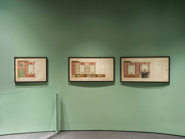 Installation. Three works on paper hang on a mint-green gallery wall. They show designs for red panelling.