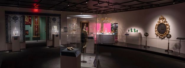 Installation. Works of art are displayed in cases, on pedestals, or hung on a wall in a dim gallery. The objects are spotlit, leaving some of the spaces in shadow.