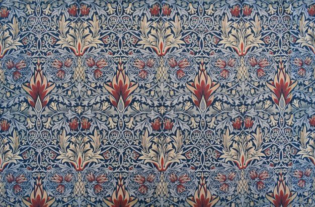 Textile. Sky-blue leaves and vines create intricate, curling patterns around cream-white, brick red, and muted pink flowers. The background is navy blue.